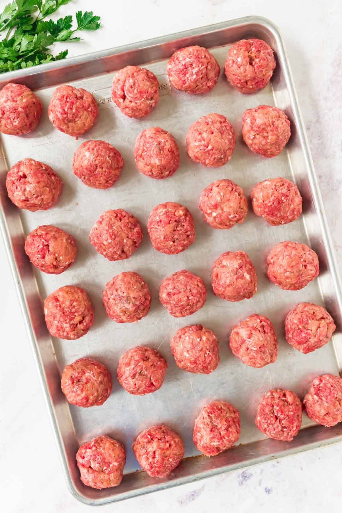 Uncooked Italian meatballs on a lined baking sheet.