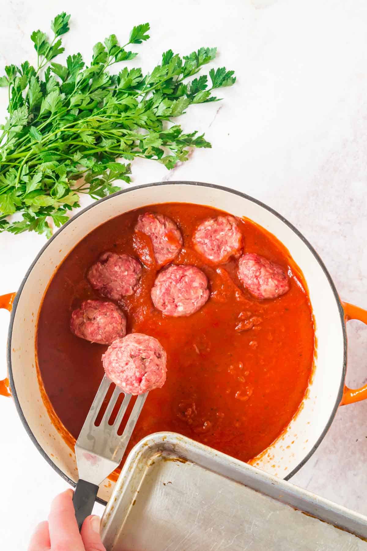 Uncooked meatballs are placed into a pot of marinara sauce.