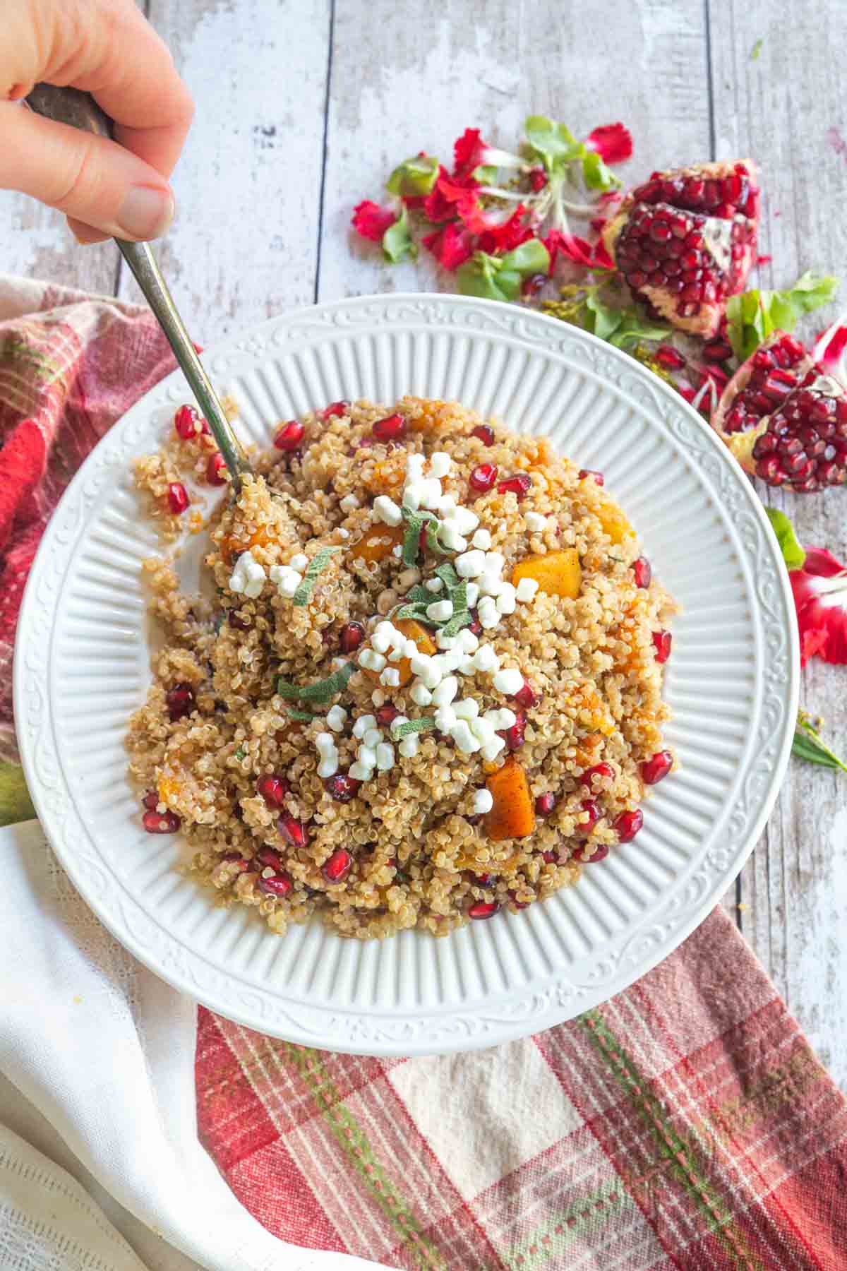 A hand holding a spoon scooping out of a bowl of butternut squash quinoa with goat cheese on top.