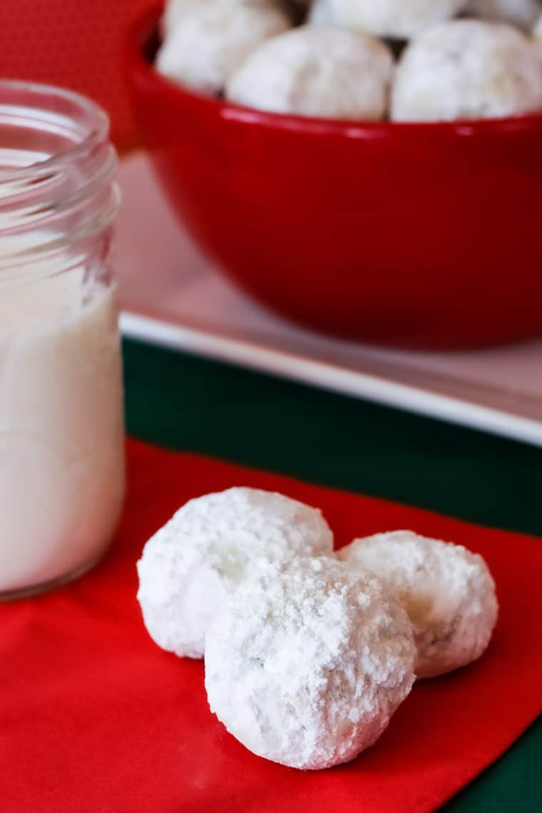 Three snowball cookies on a red napkin with a bowl of more snowballs