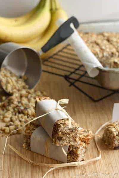 A stack of wrapped banana nut breakfast granola bars next to a oats spilling from a measuring cup.