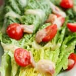 Plated romaine wedge with tomatoes and bacon dressing on a white plate.