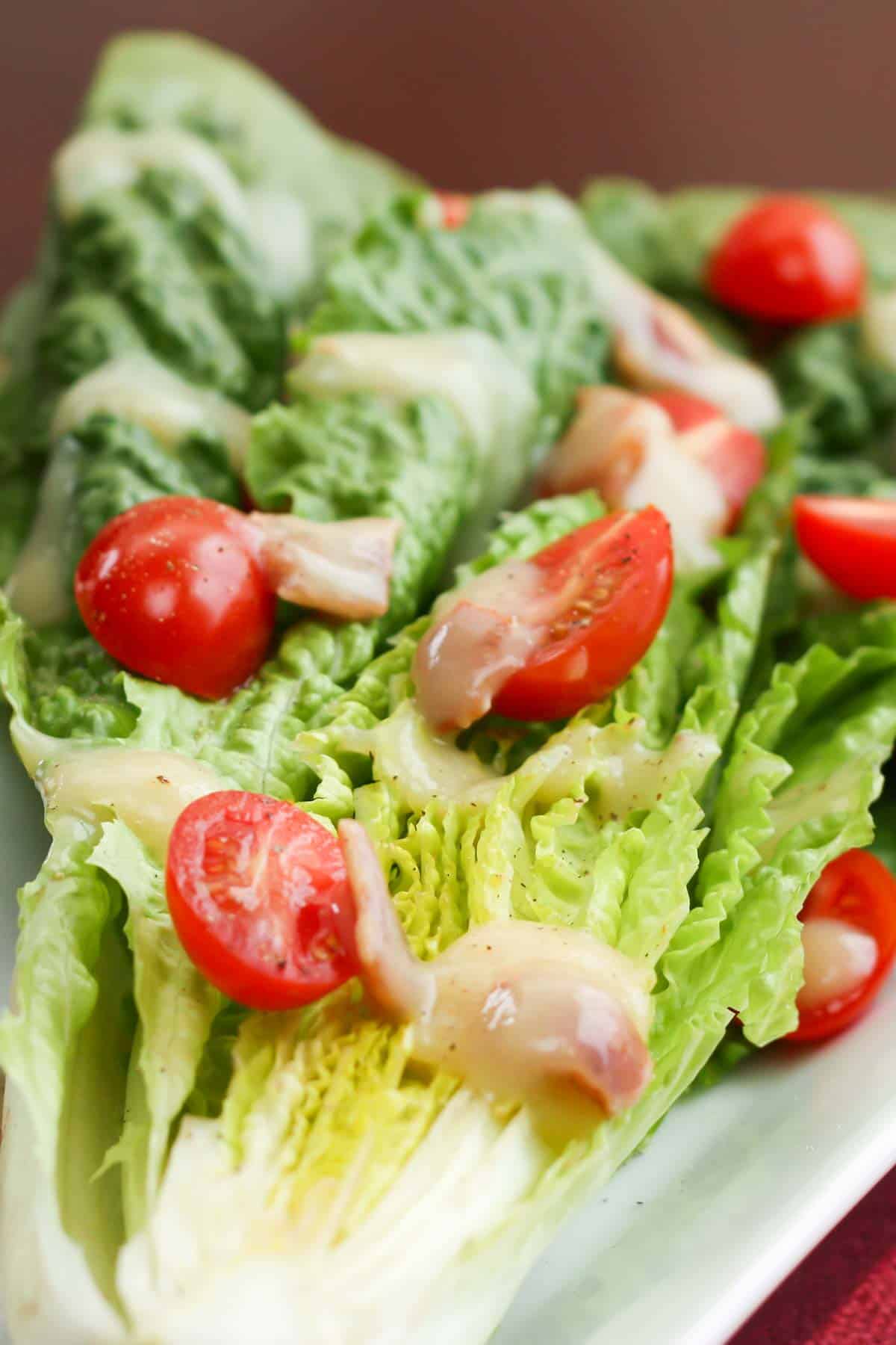 Plated romaine wedge with tomatoes and bacon dressing on a white plate.