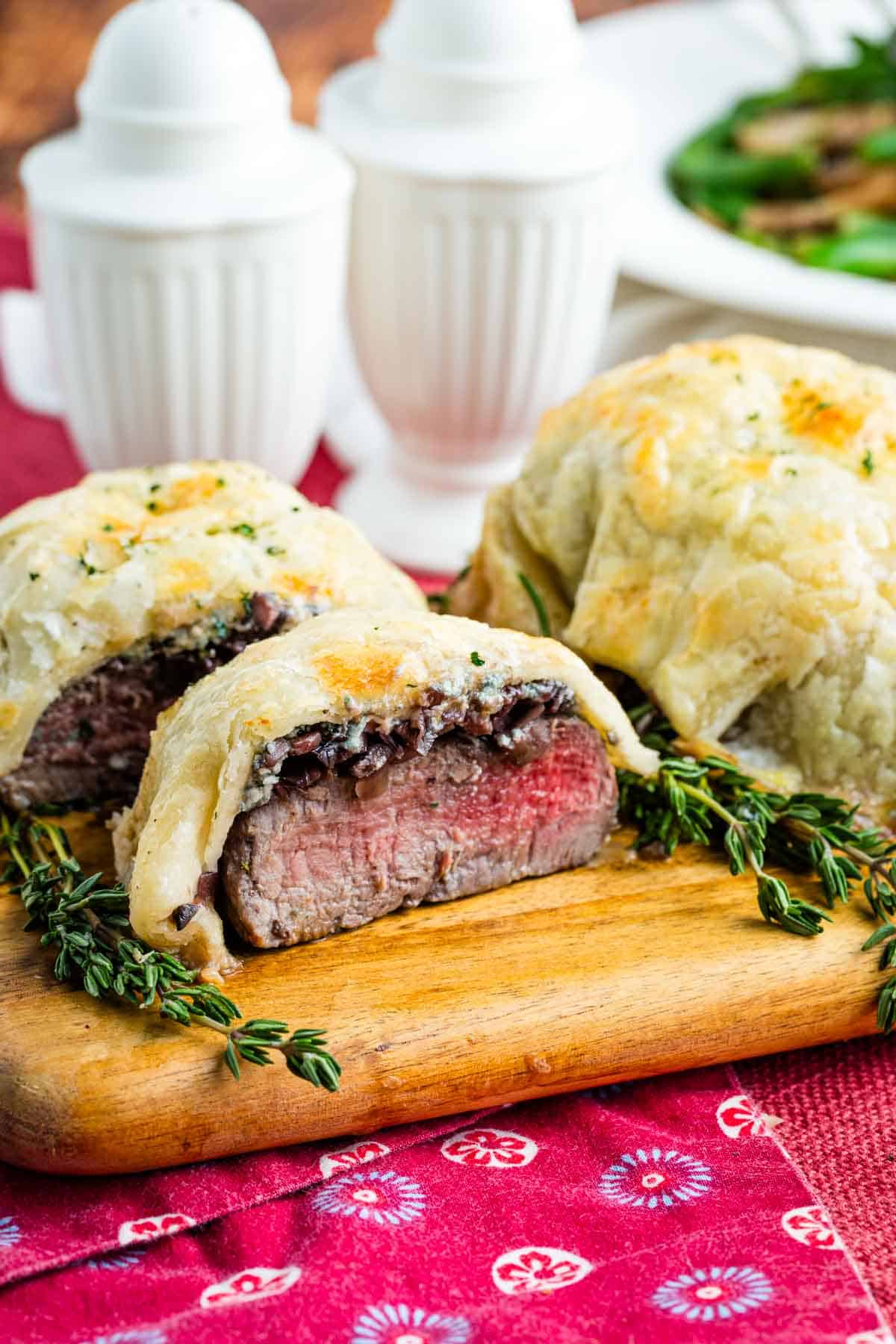 Individual Beef Wellingtons on a cutting board, one cut in half to show the inside