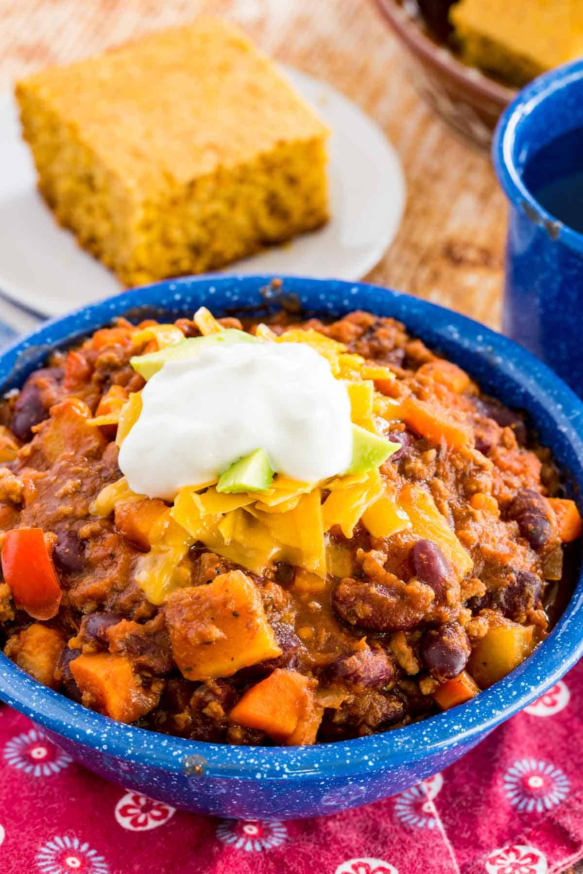 Slow cooker Aloha chili in a bowl topped with sour cream, with cornbread in the background.