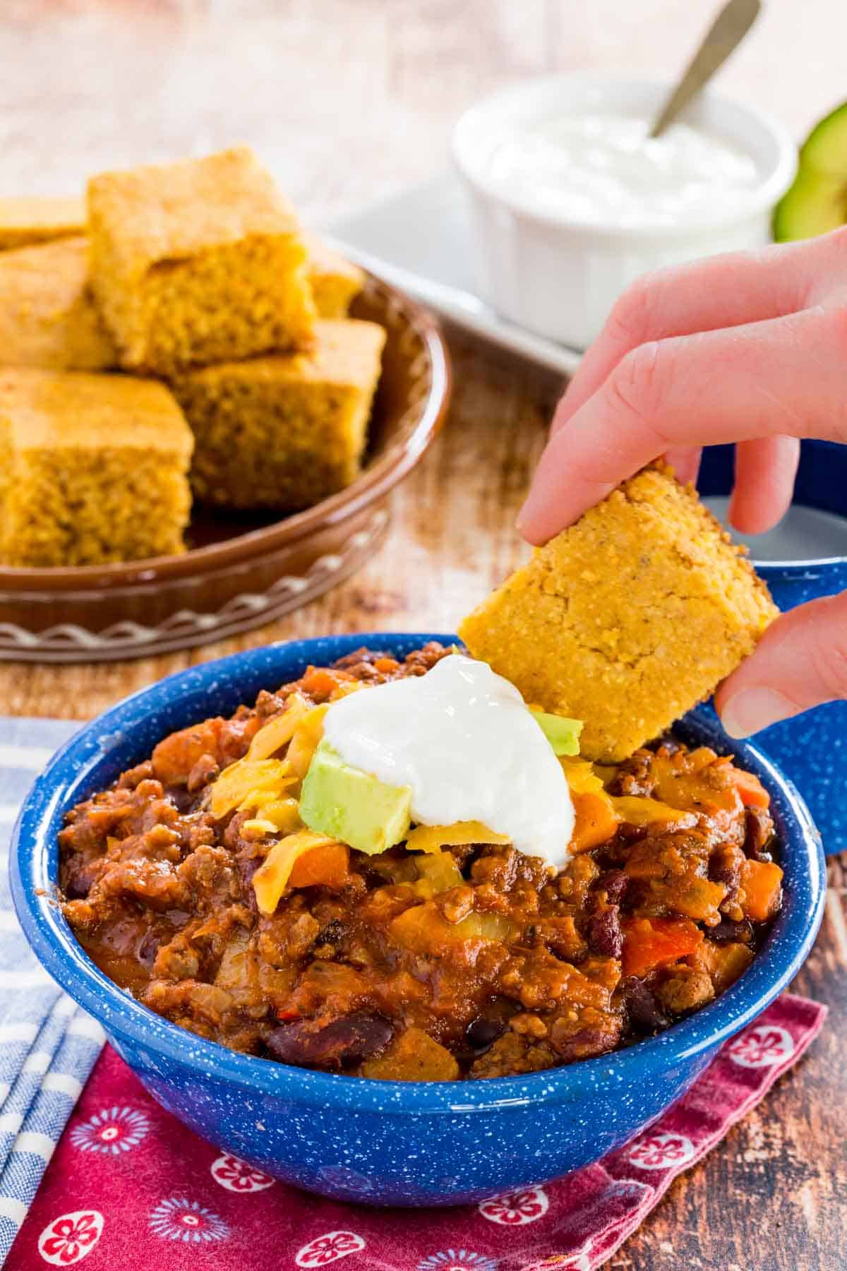 Cornbread is dipped into slow cooker chili topped with sour cream.