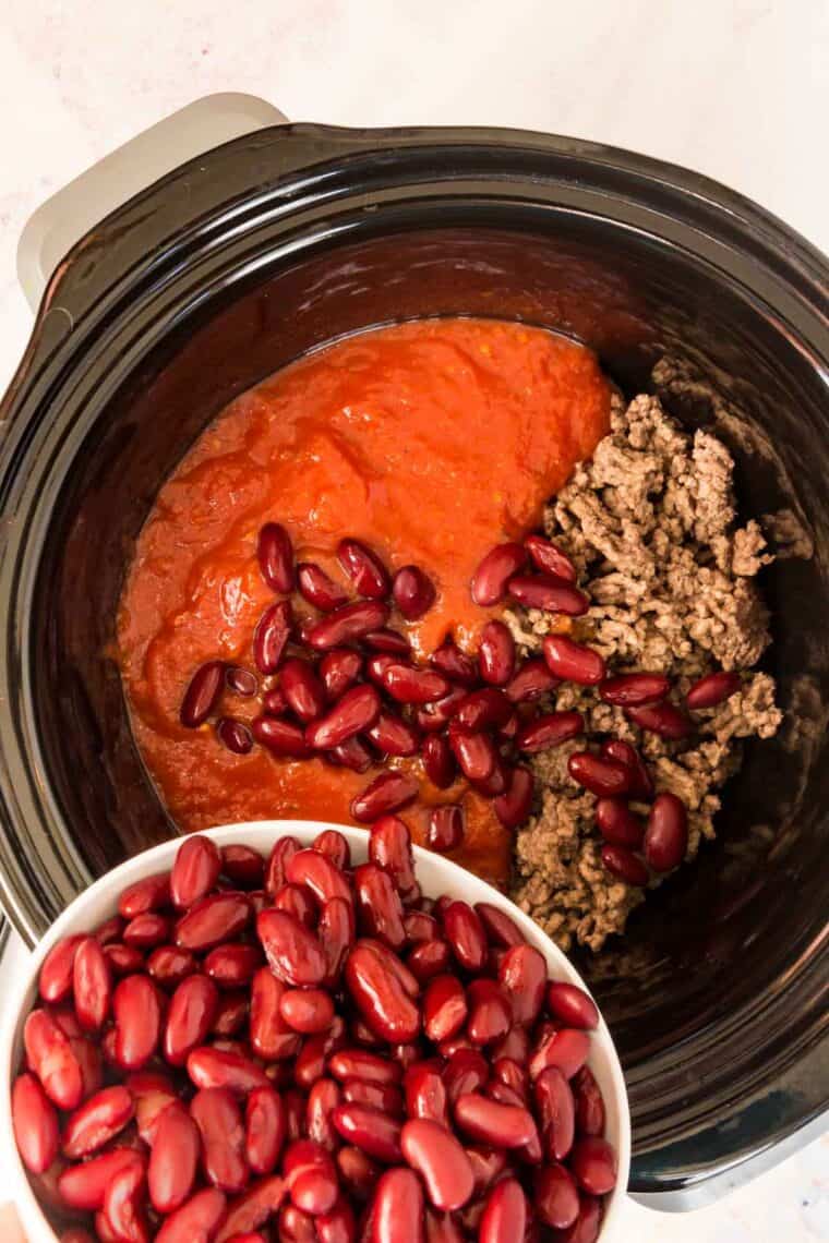 Beans are added into the slow cooker with tomatoes and ground beef.