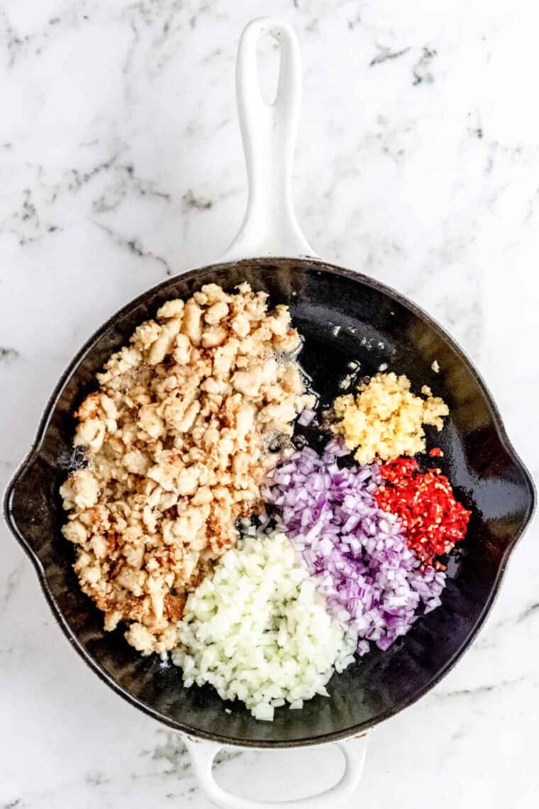 Onions, shallots, garlic, and chilies added to one side of a skillet, with browned chicken on the other.