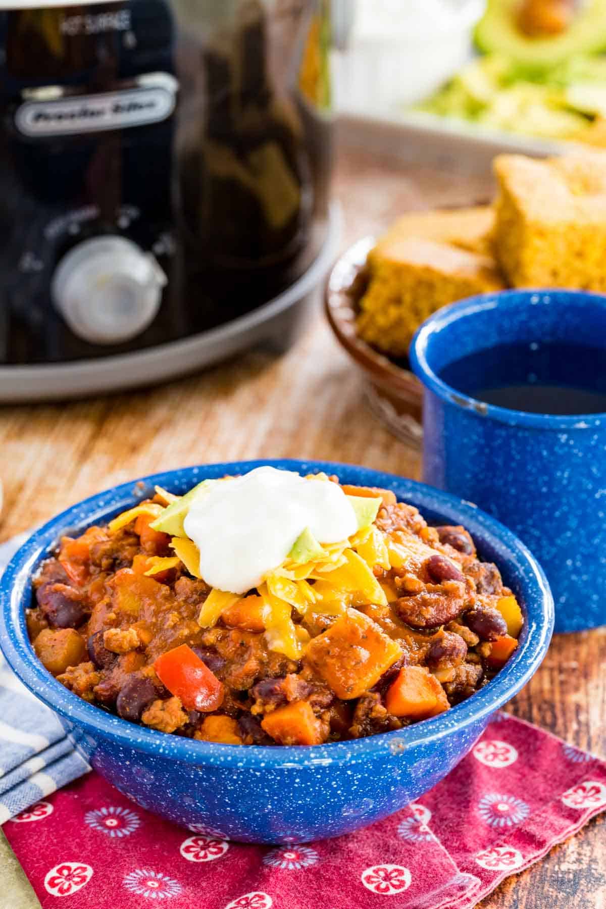 Slow cooker Aloha chili in a bowl topped with sour cream, with cornbread in the background.