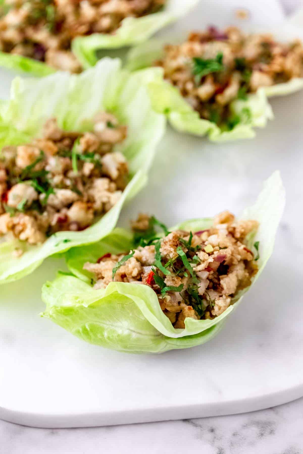 Thai larb chicken lettuce wraps on a white stone cutting board.