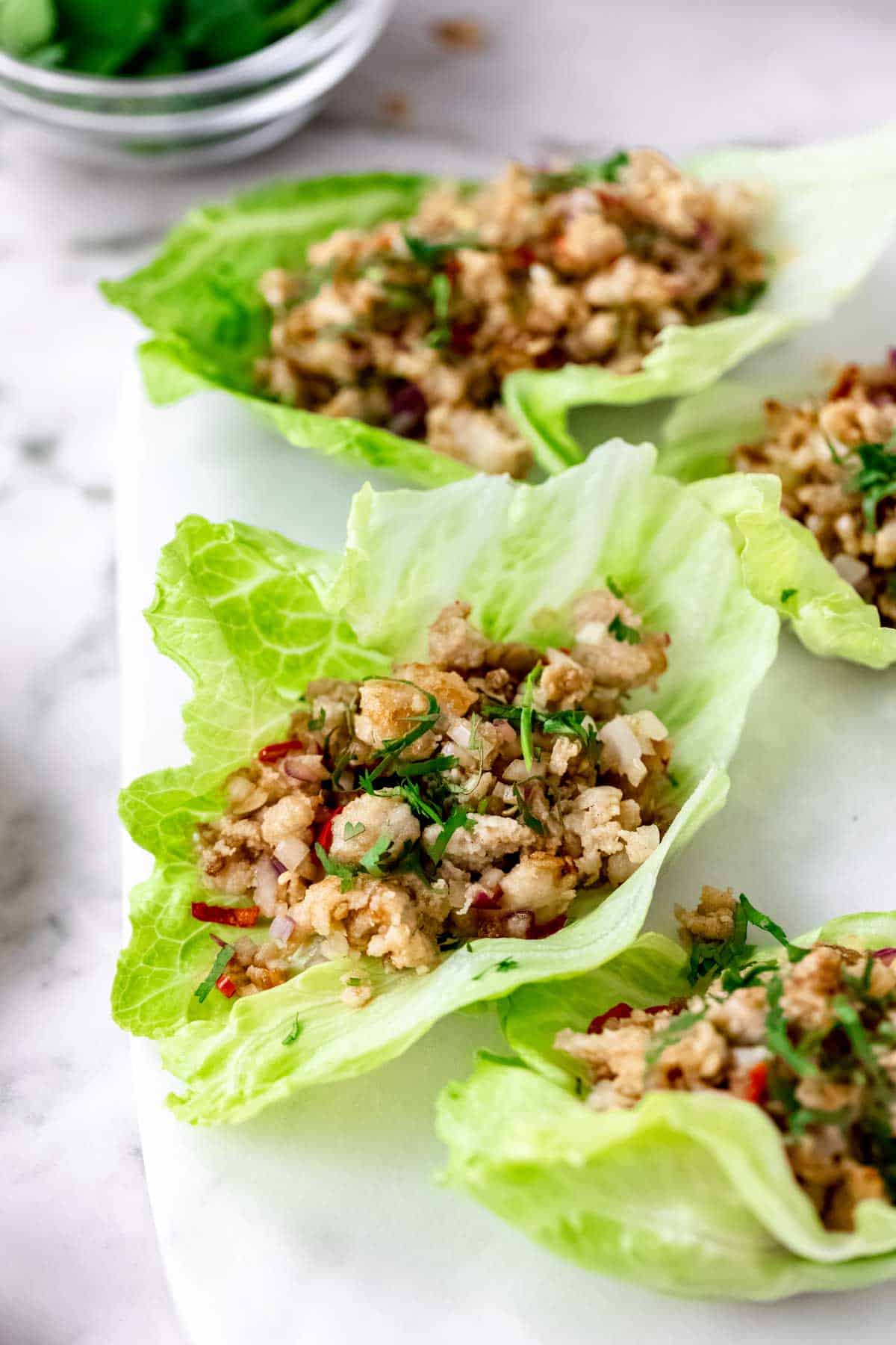 Close up of Thai larb chicken lettuce wraps on a white stone cutting board.