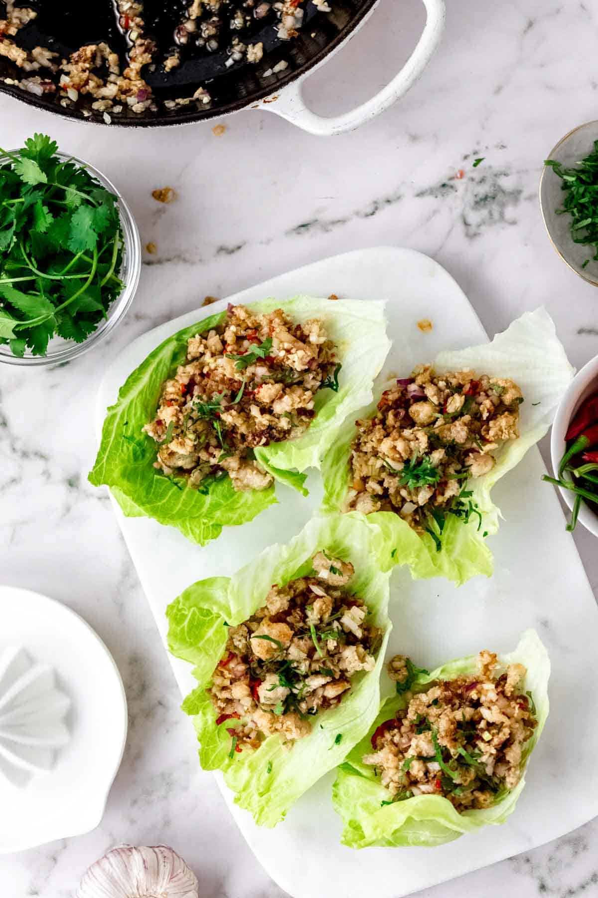 Overhead view of Thai larb chicken lettuce wraps on a white stone cutting board, next to a skillet.