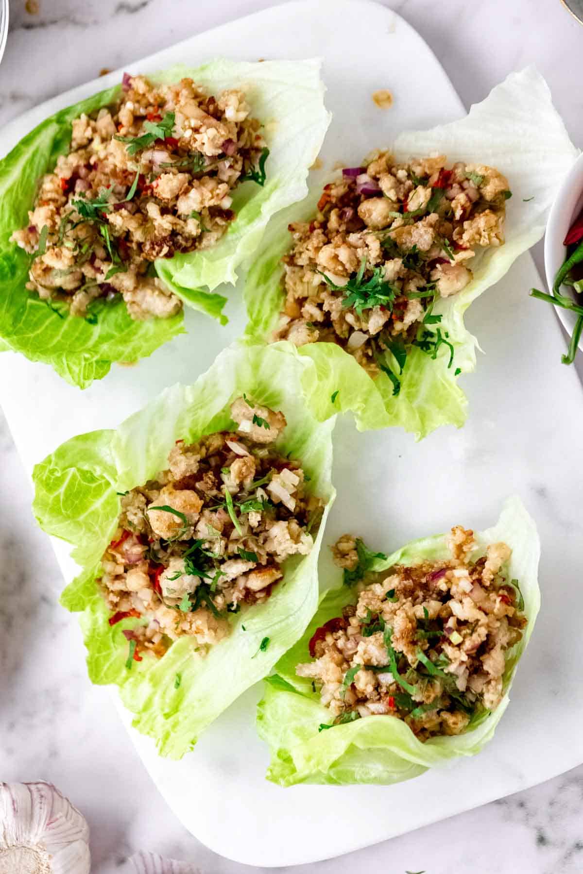 Overhead view of Thai larb chicken lettuce wraps on a white stone cutting board.