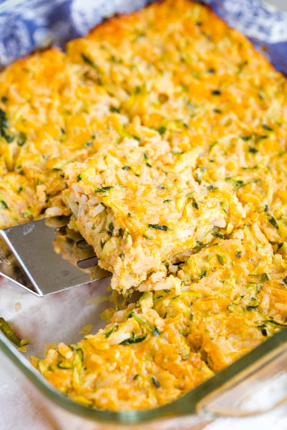 Scooping up a piece of zucchini rice casserole out of the baking dish