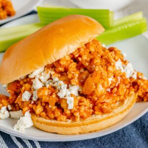 Ground chicken mixture spilling off the sides of a buffalo chicken sandwich on a roll.