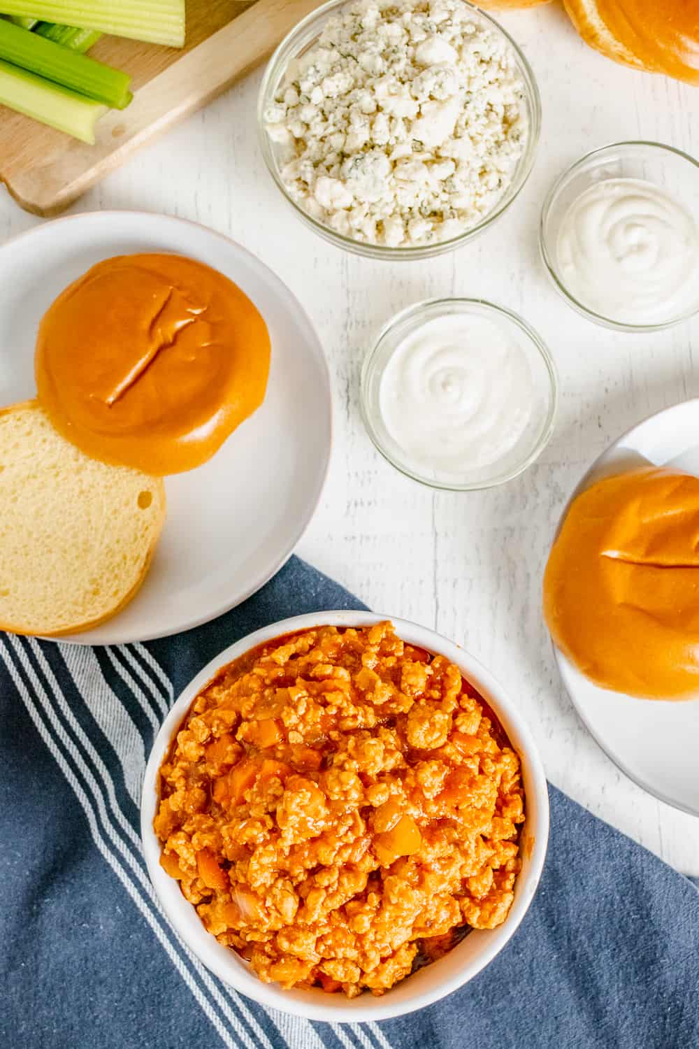 Buffalo chicken sloppy joes ground chicken mixture in a bowl with rolls nearby on plates and blue cheese and ranch dressing in bowls