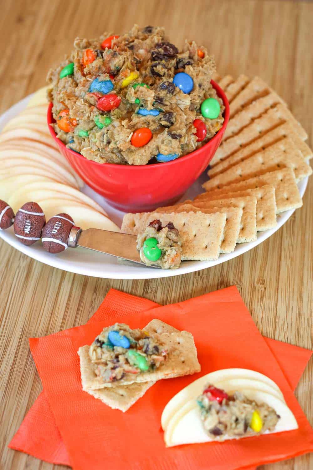 A bowl of monster cookie dough dip on a plate with graham crackers and apple slices with the dip on some of these items on a napkin.