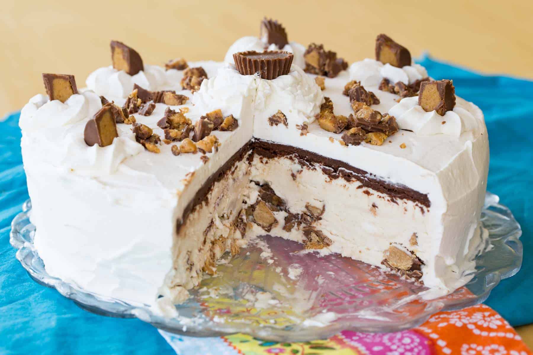 A Reese's ice cream cake on a platter with a slice removed to show the layers.