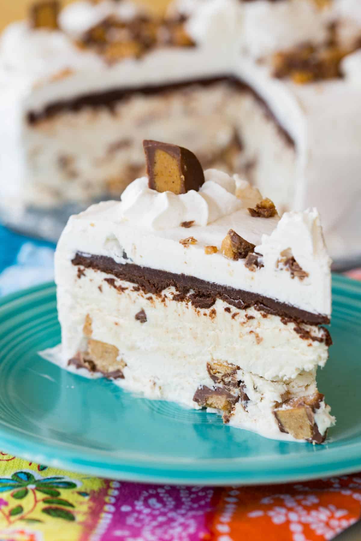 A slice of Reese's peanut butter ice cream cake on a plate with the rest of the cake behind it.