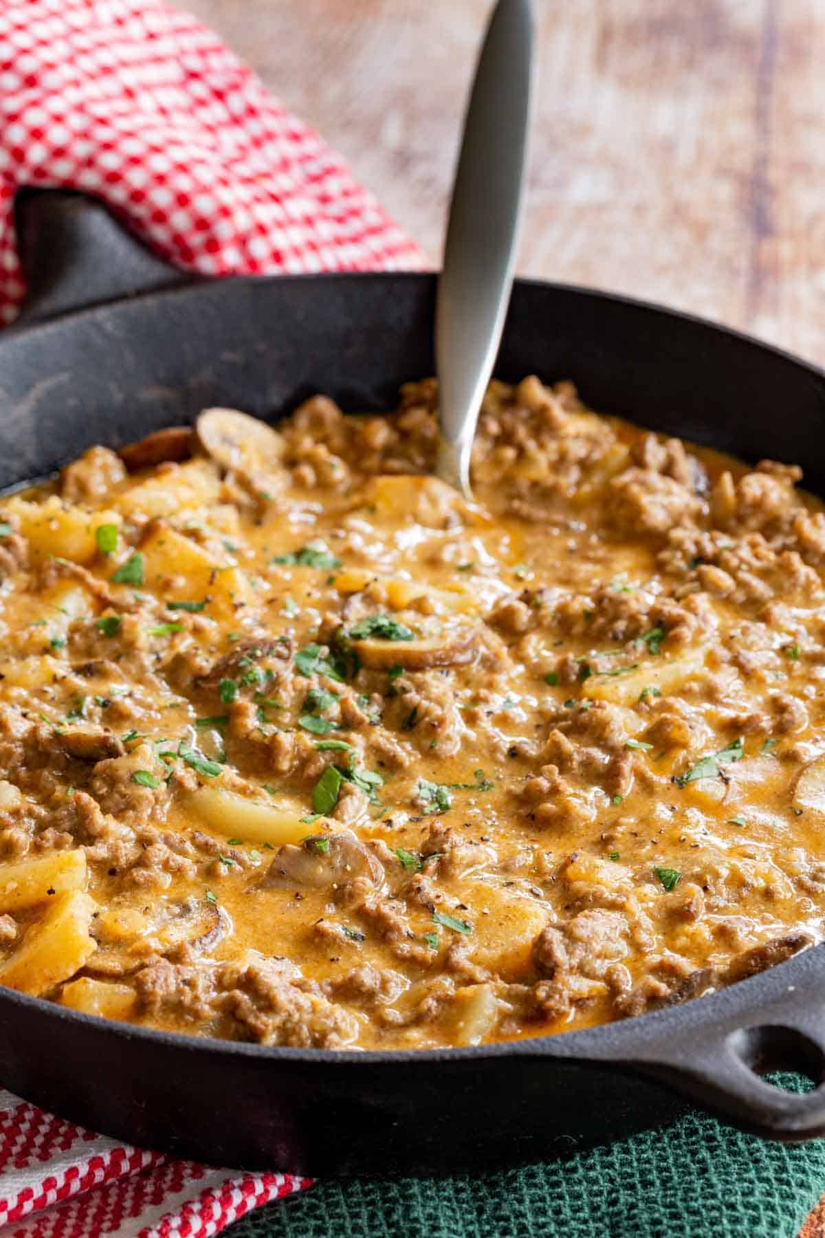 One Pan Ground Beef and Potatoes Recipe in a Cast Iron Skillet with the handle being held by a red and white oven mitt.