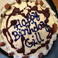 ice cream cake with chocolate drizzles and icing that says "Happy Birthday Gill"