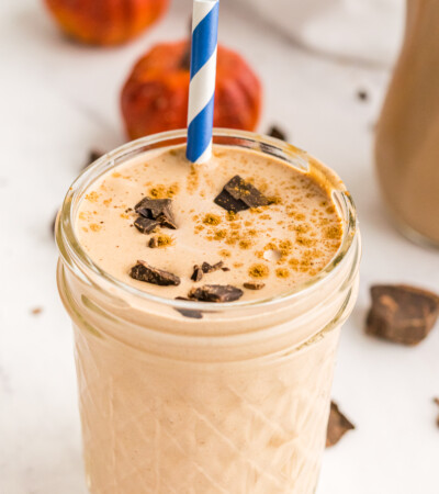 A Chocolate Pumpkin Smoothie in a jelly jar with a sprinkle of pumpkin pie spice and bits of chocolate on top and a blue and white striped straw