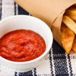 A paper cone of FrenchFries with a bowl of homemade ketchup
