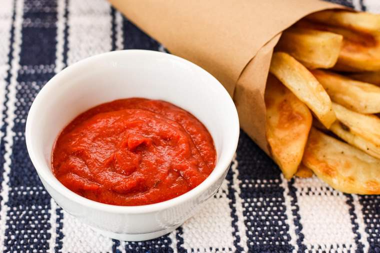 A paper cone of French Fries with a bowl of homemade ketchup