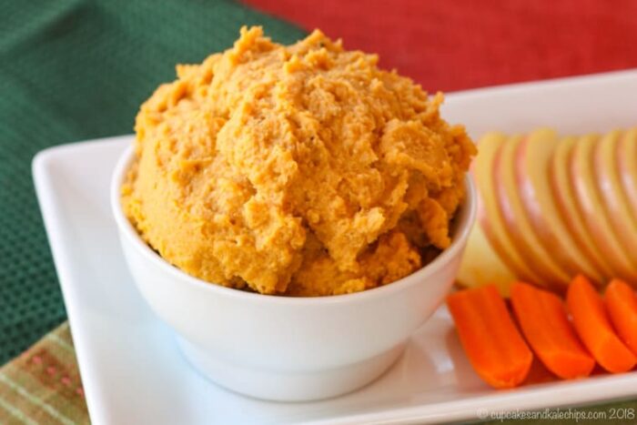 A bowl of Maple Walnut Sweet Potato Hummus on a platter with carrots and apples