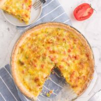 Turkey swiss quiche in a glass pie plate with a piece cut out and on a plate