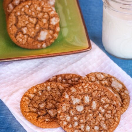 Gingersnap cookies on a white napkin with a glass of milk