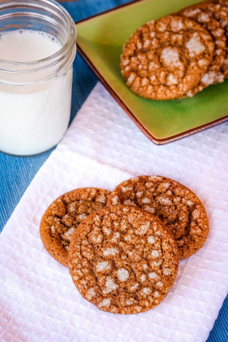 Three gingersnap cookies on a white napkin with more on a green plate