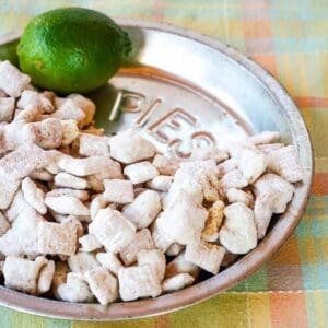 White chocolate puppy chow snack mix in a metal pie plate with a lime.