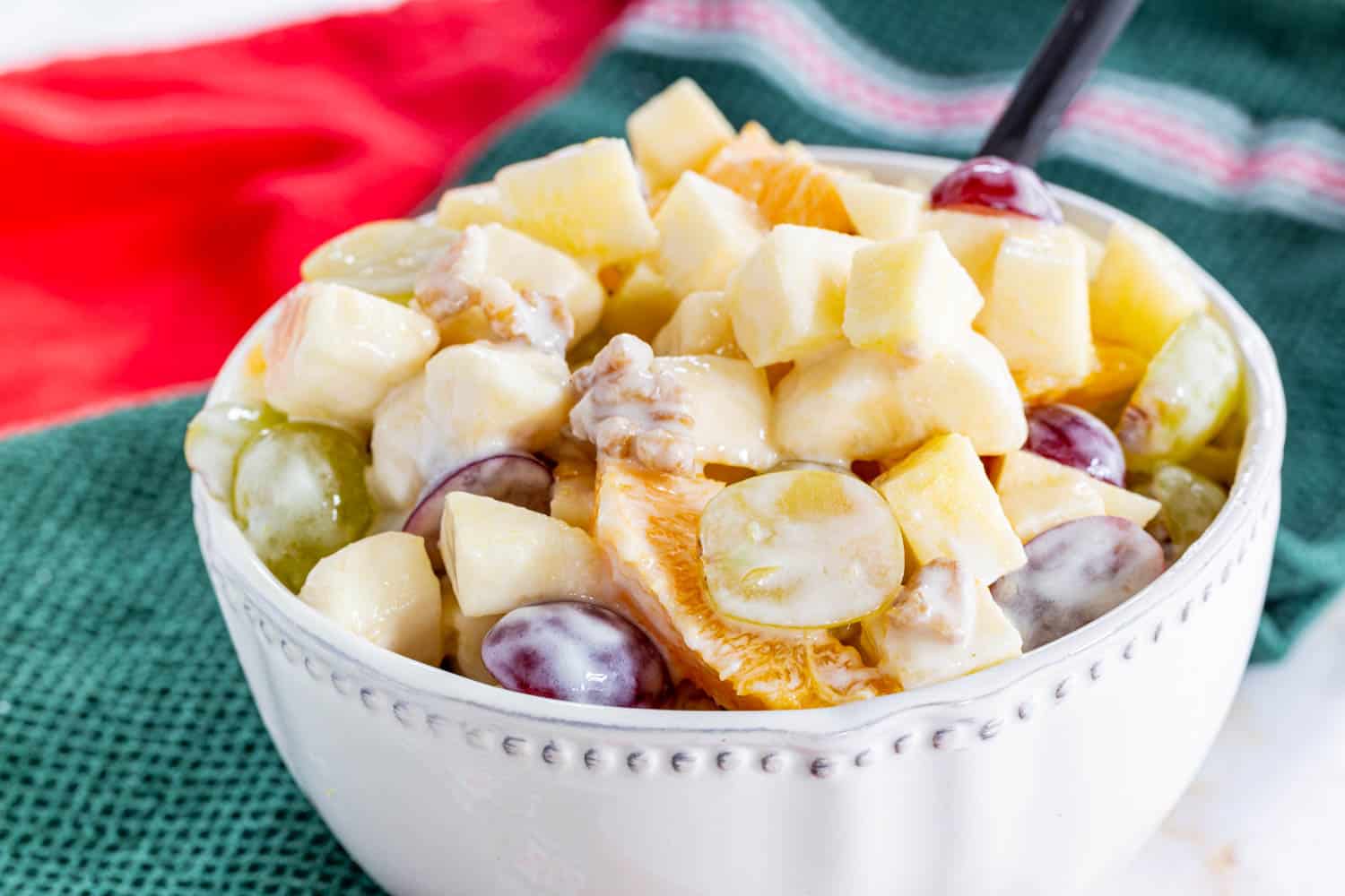 Winter Fruit Salad with apples, grapes, oranges, bananas, and walnuts in a bowl on top of red and green cloth napkins.