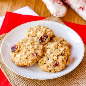 Cranberry white chocolate oatmeal cookies on a white plate on top of a piece of burlap and a red napkin.