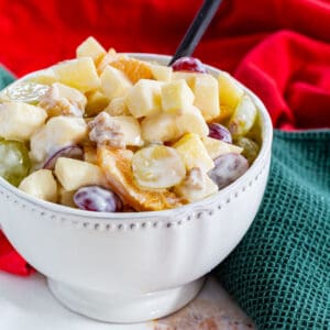 A bowl of fruit salad with apples, graped and oranges coated in a creamy dressing.