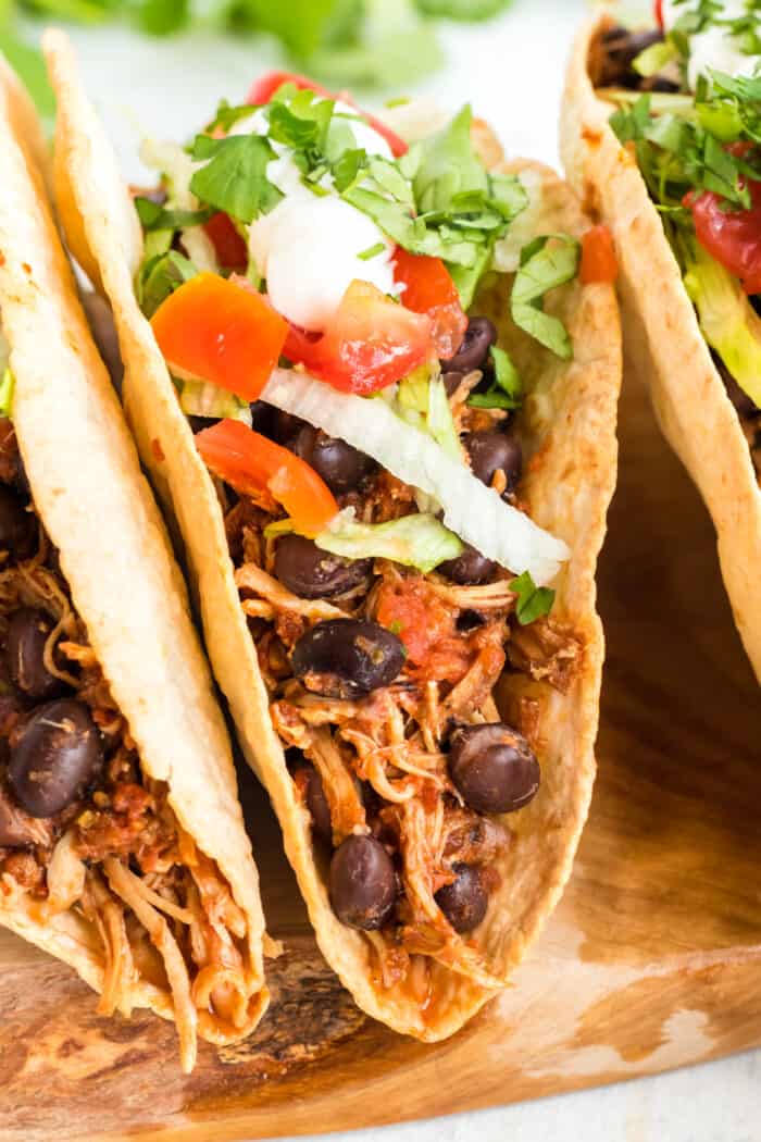 Tacos filled with shredded chicken, black beans, lettuce, tomatoes, and sour cream