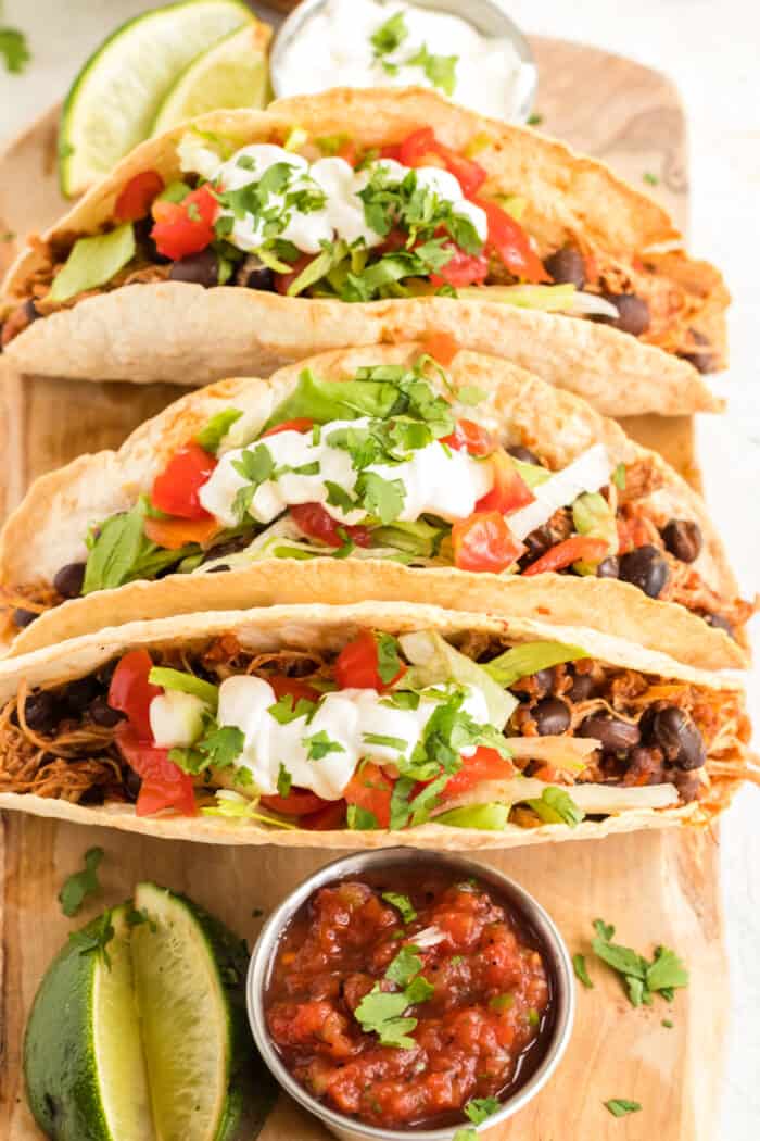 Three chicken black bean tacos on a cutting board with a bowl of salsa