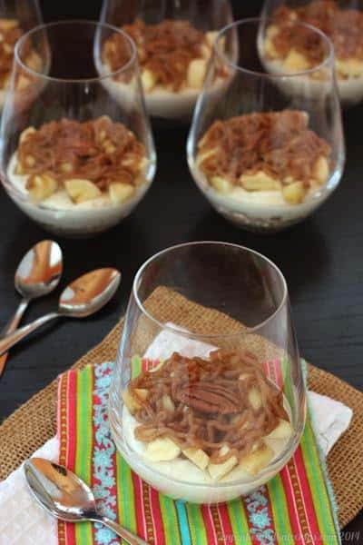 A bananas foster cheesecake parfait in a glass, with parfaits in the background.