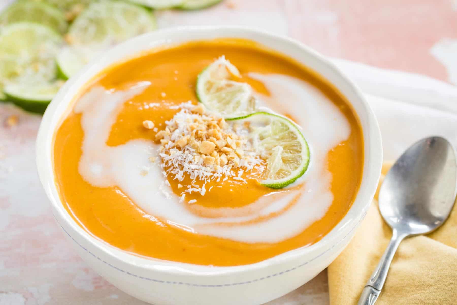 Thai Curry Butternut Squash Soup served in a bowl with soup spoon and garnishes of peanuts and coconut on top.