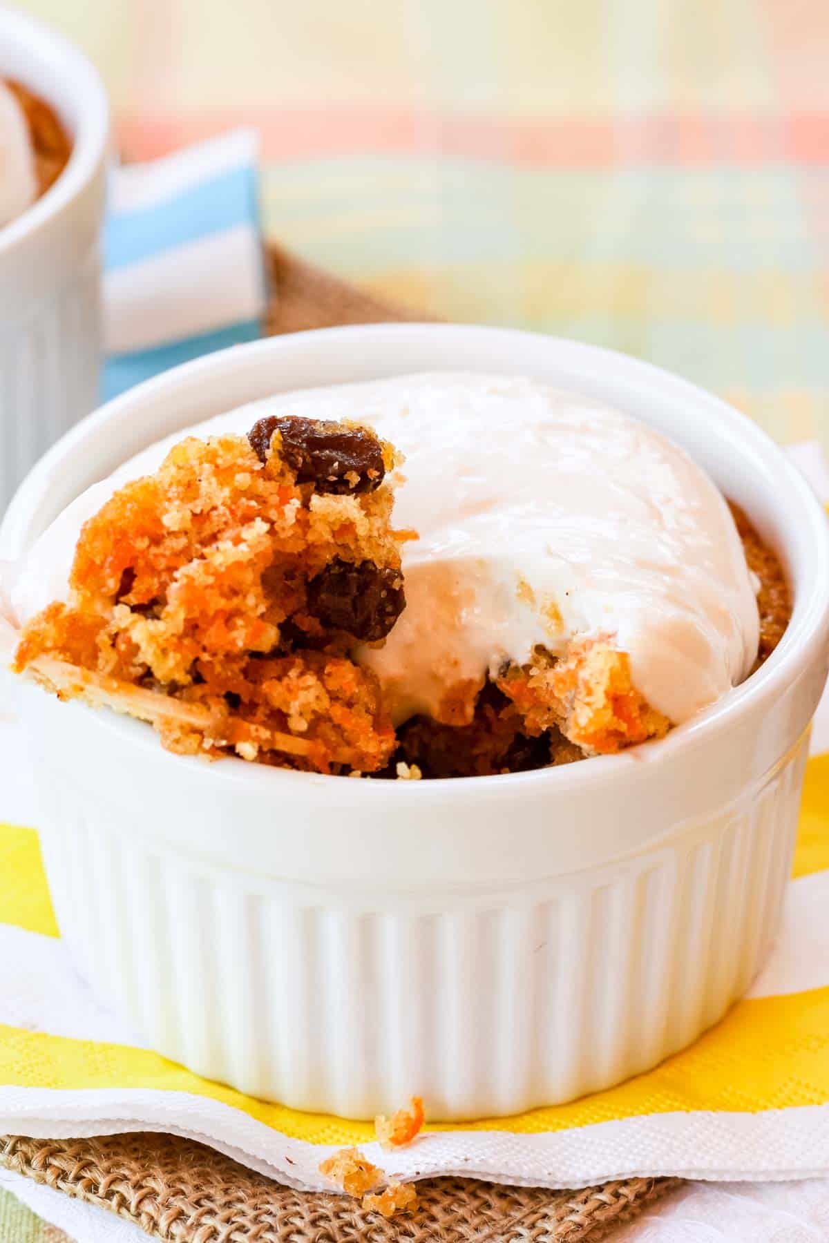 A spoon resting on the side of a ramekin fill of carrot cake with cream cheese frositng.
