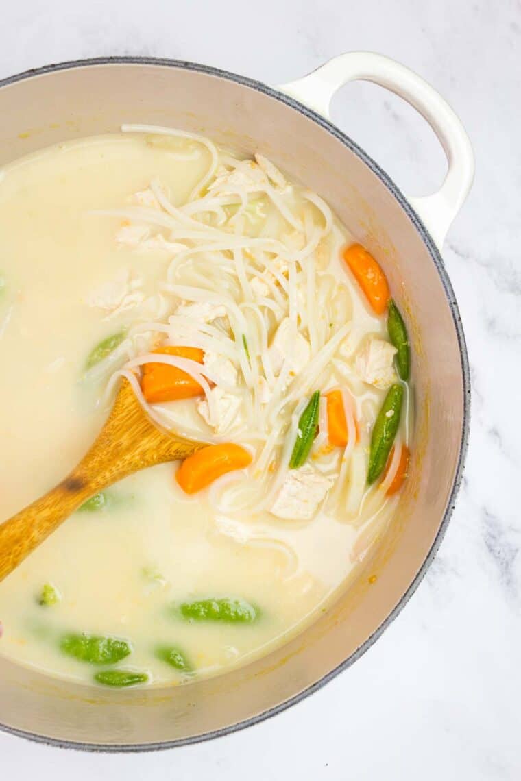 A wooden spoon in a pot of Thai chicken noodle soup