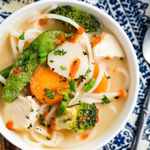 Overhead view of a bowl of Thai chicken noodle soup topped with a drizzle of sriracha