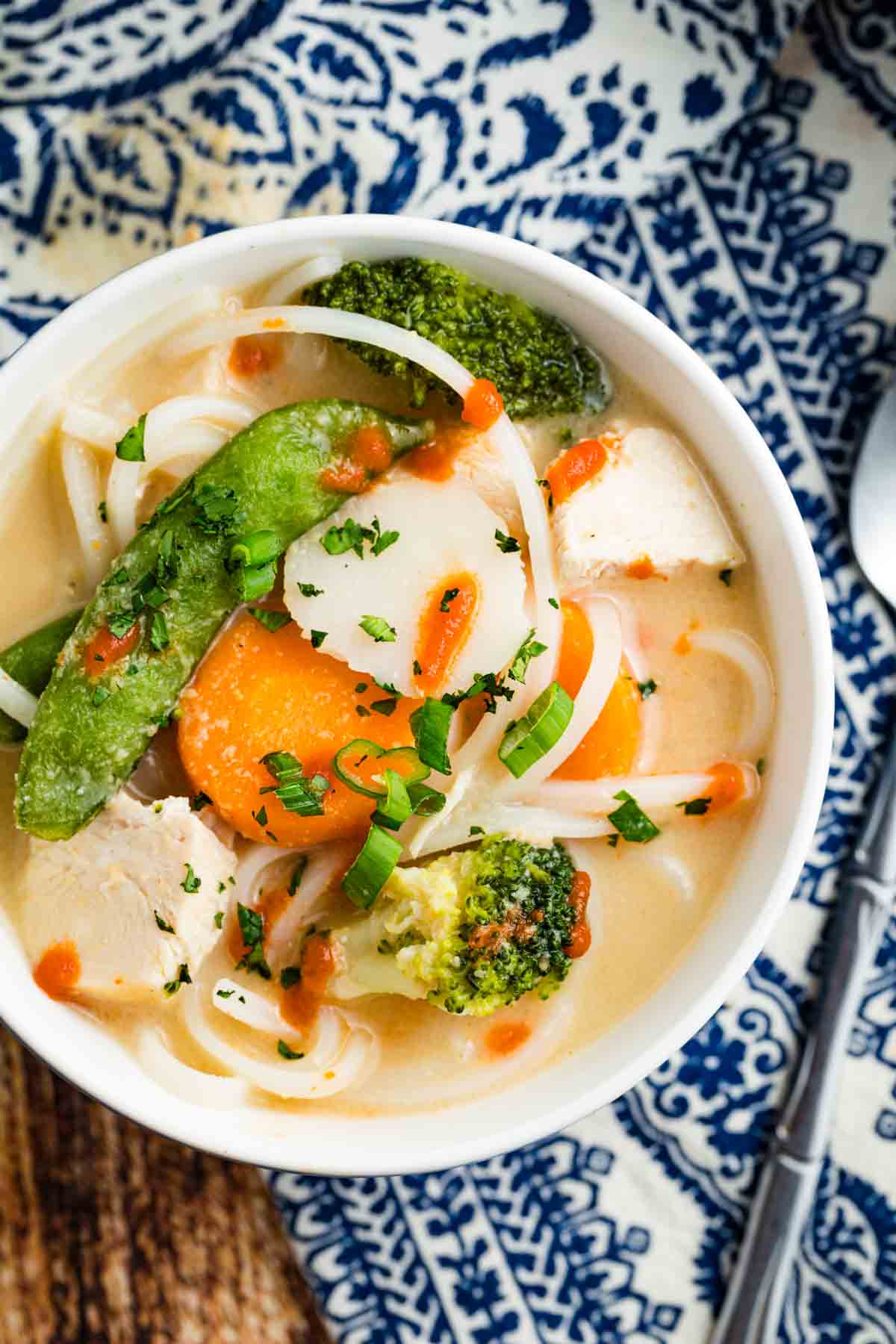 Overhead view of a bowl of Thai chicken noodle soup topped with a drizzle of sriracha