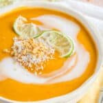 Closeup of a bowl of curry butternut squash soup with lime, coconut, and peanut garnish.