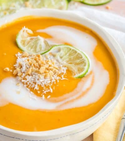 Closeup of a bowl of curry butternut squash soup with lime, coconut, and peanut garnish.