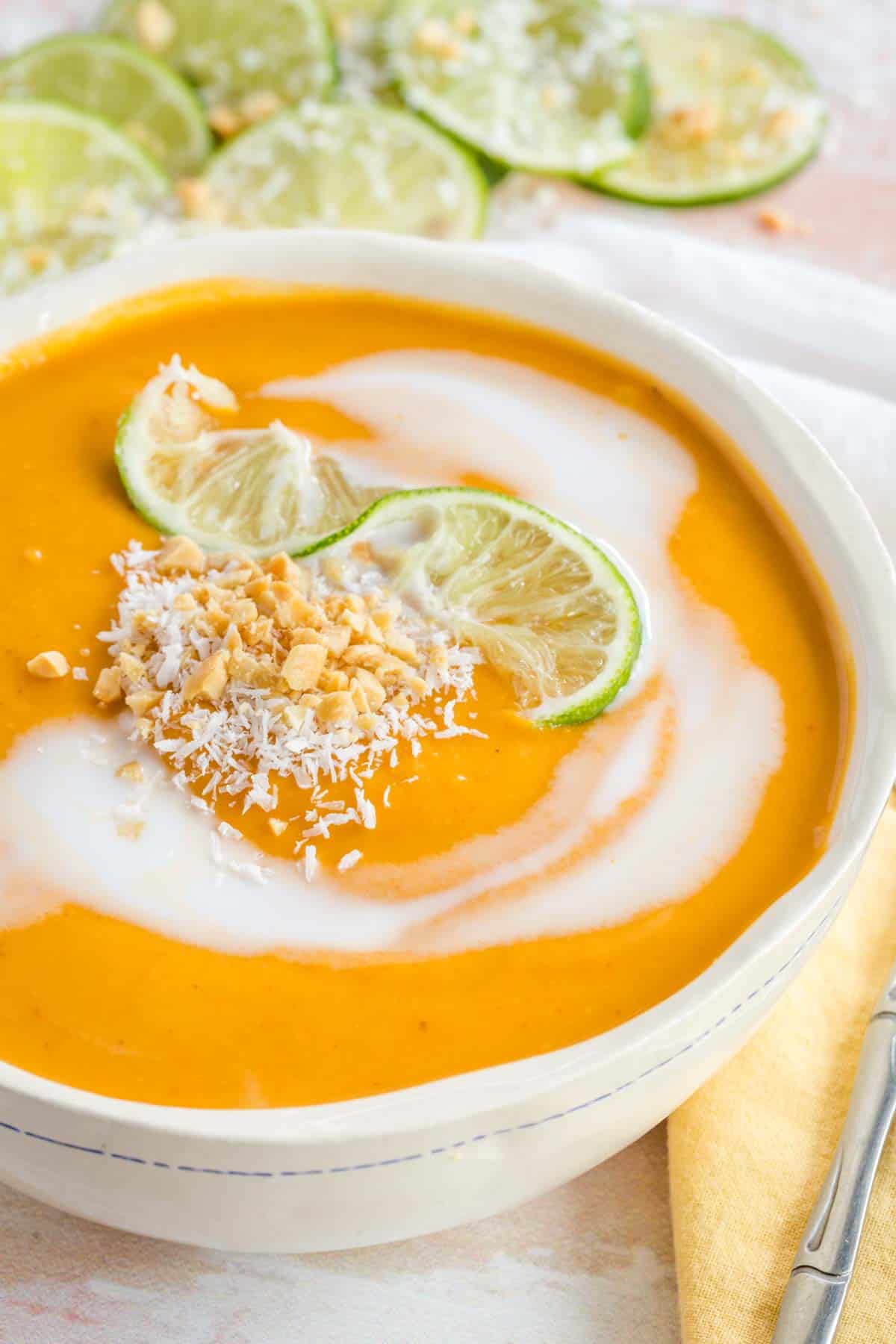 Closeup of a bowl of curry butternut squash soup with lime, coconut, and peanut garnish.