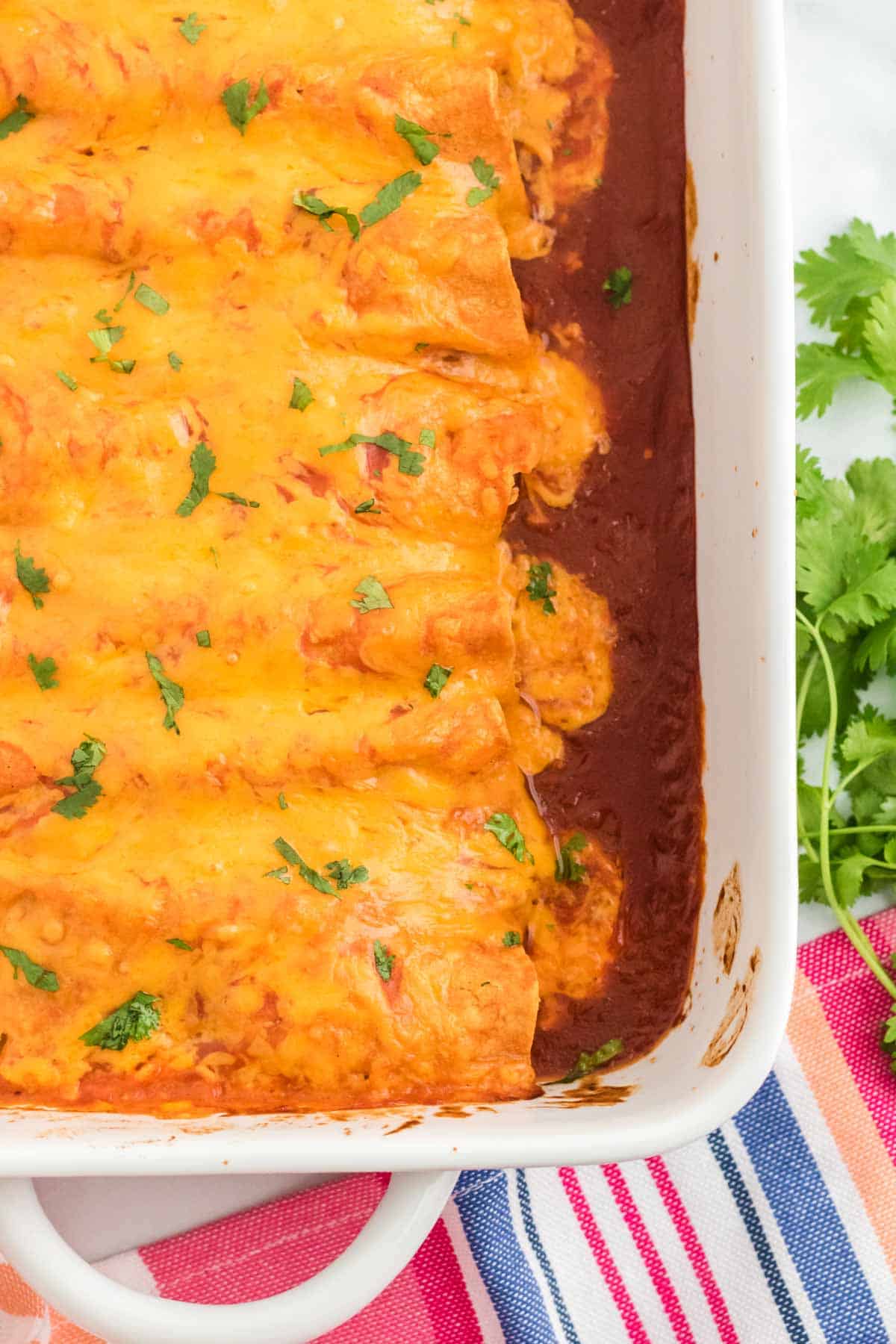 The corner of a baking dish filled with cheesy chicken enchiladas.