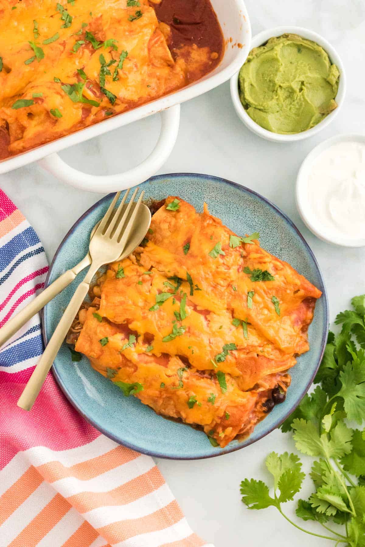 Cheesy chicken enchiladas on a plate next to garnishes.