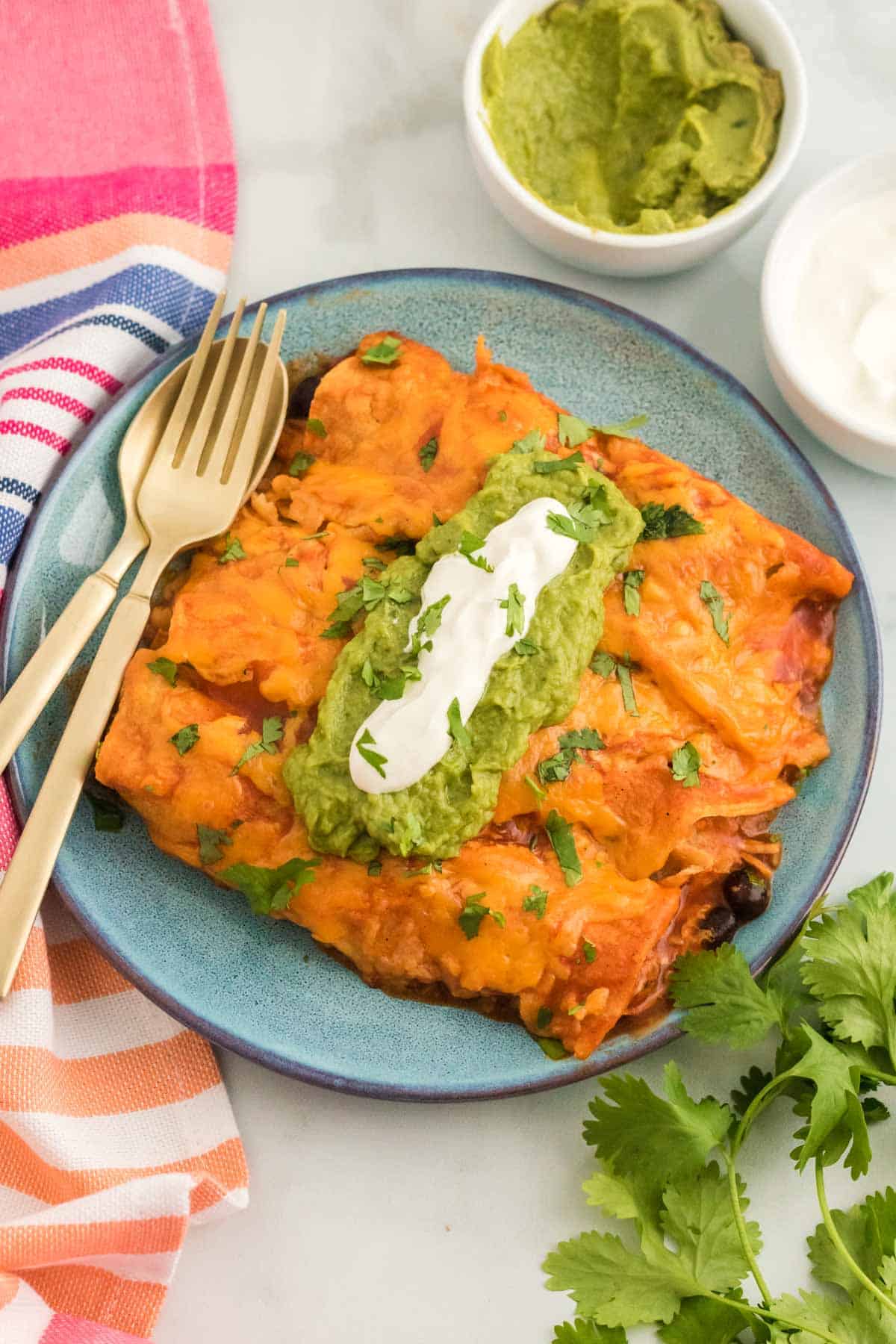 Chicken enchiladas garnished with guacamole and sour cream on a plate next to a fork.